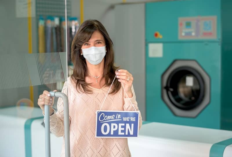 business owner at a laundromat putting an open sign while wearing a facemask cm 1